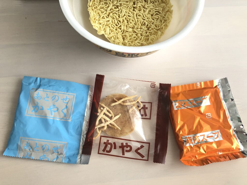カップ麺「銀座香味徳監修　鳥取ゴールド牛骨ラーメン」の蓋を開け、中身のかやく、あとのせかやく、液体スープが出てきた写真